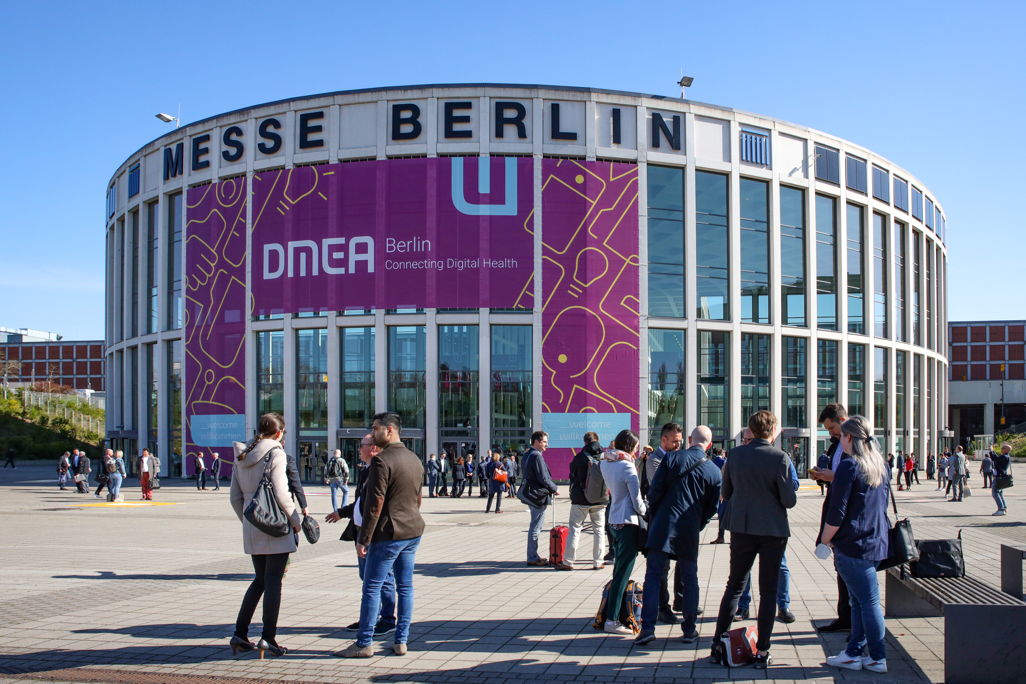 Menschen vor dem Südeingang der Messe Berlin. Auf dem Eingang ist ein Banner der DMEA zu sehen.