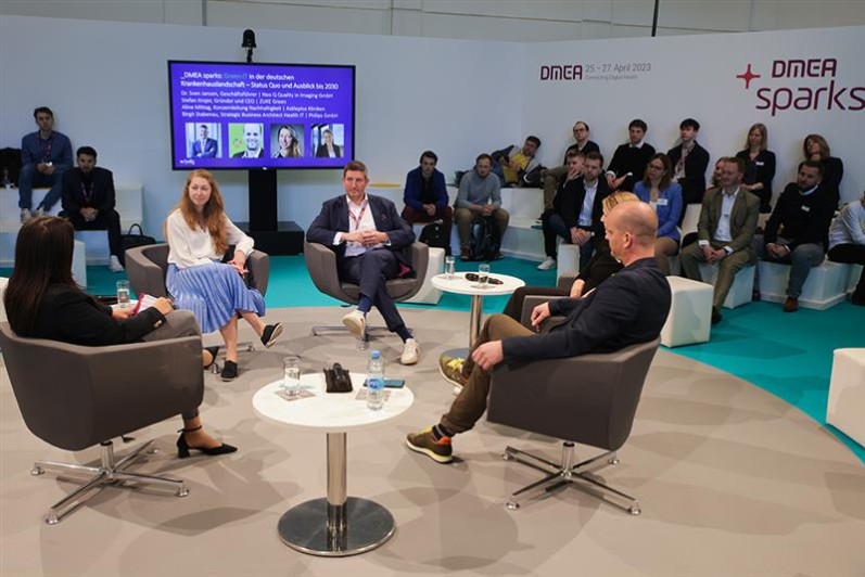 Vier Personen bei einer Panel-Diskussion, rundum sitzt Publikum. Vier Personen bei einer Panel-Diskussion, rundum sitzt Publikum.