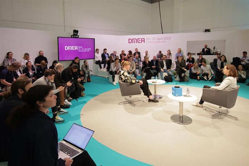 Zwei Frauen sitzen auf zwei Sesseln in einer der DMEA Boxen, um sie herum sitzt Publikum. Zwei Frauen sitzen auf zwei Sesseln in einer der DMEA Boxen, um sie herum sitzt Publikum.