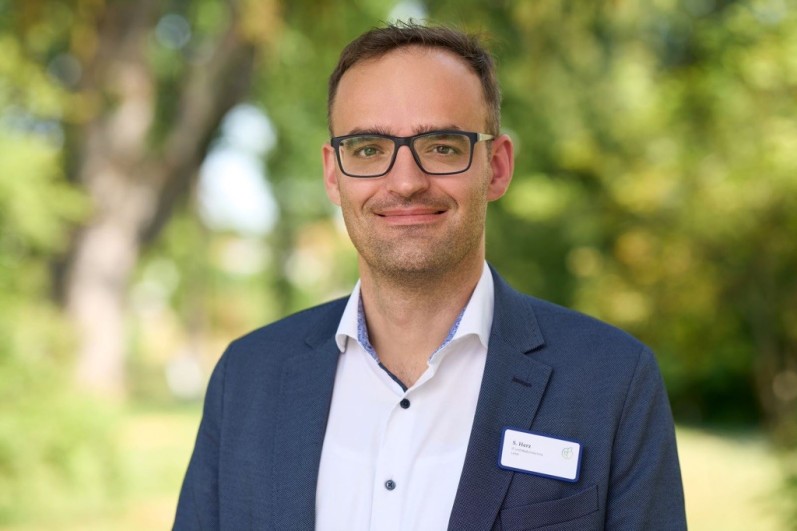 Mann mit Brille, trägt Anzug, im Hintergrund sind Bäume zu sehen. Mann mit Brille, trägt Anzug, im Hintergrund sind Bäume zu sehen.