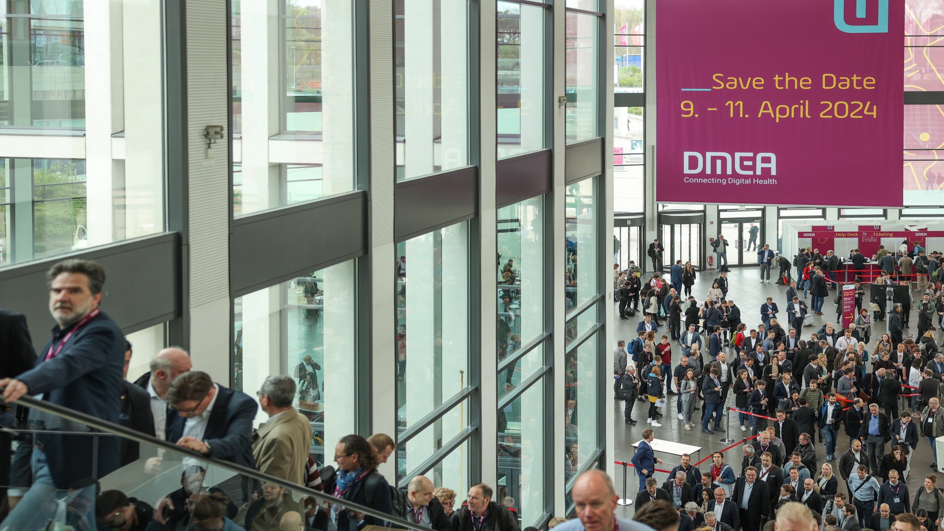 Besucher:innen auf dem Weg in die Messehallen; Save the Date-Schild zur DMEA 2024 