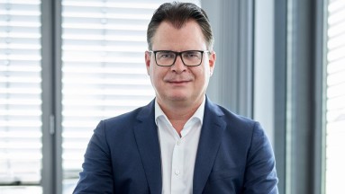 Man with dark blue jacket, white shirt and black glasses.