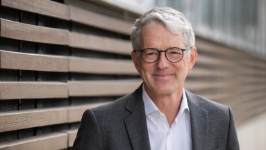 Man with glasses wears grey jacket and white shirt.