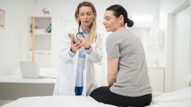 Eine Ärztin hält ein Tablet in ihrer rechten Hand und zeigt ihrer Patientin mit der anderen Hand etwas auf dem Bildschirm.