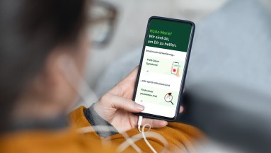 A woman looks at her smartphone, which shows the welcome page of the AOK portal.