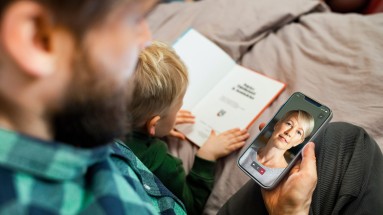 Vater und Sohn schauen auf ein Smartphone, auf dem eine Frau zu sehen ist.