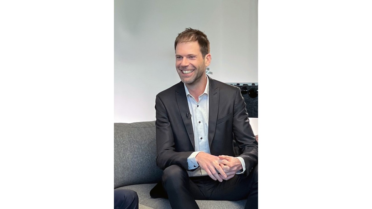 Man in grey suit sitting on a sofa.