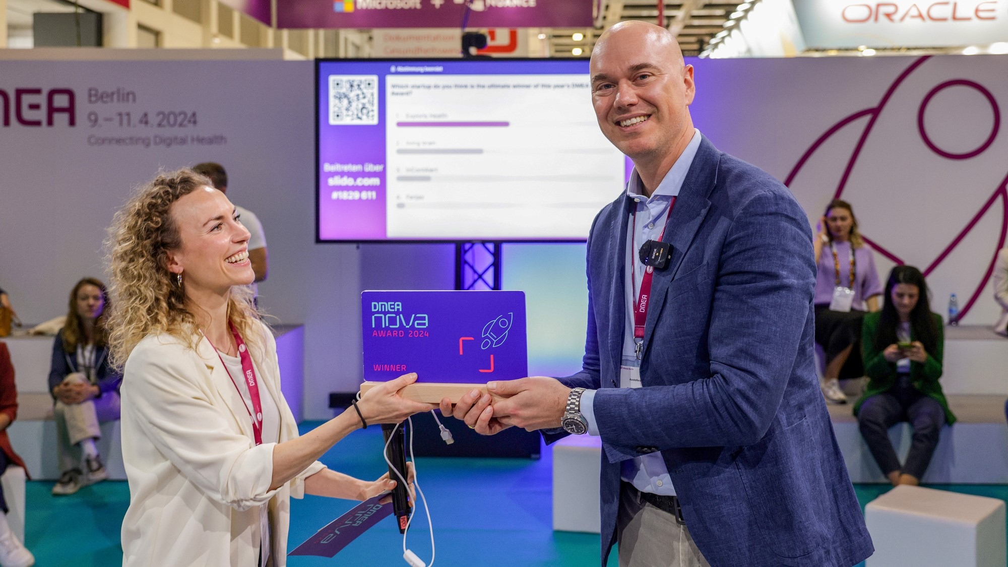 Verleihung des DMEA nova Award auf der DMEA 2024. Links steht eine Frau, die den dunkelblauen Award an den Mann rechts überreicht. Verleihung des DMEA nova Award auf der DMEA 2024. Links steht eine Frau, die den dunkelblauen Award an den Mann rechts überreicht.