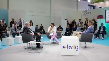 Three people are sitting in an open discussion circle on a stage and holding a conversation.