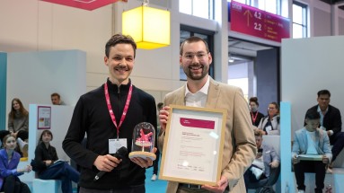 Julian Hugo, Gewinner DMEA sparks Awards 2024, hält einen Pokal, neben Marco Florian Aigner, der eine Urkunde hält. 