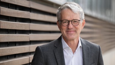 Portrait of Matthias Meierhofer in a suit in front of a wall with wooden beams 