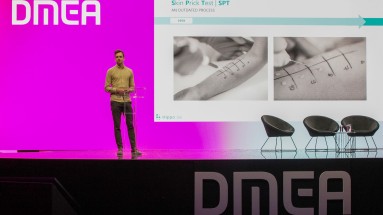 A person is standing on a stage at DMEA 2025 and giving a presentation.