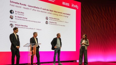 Four people are standing on a stage in front of a large screen displaying the title “Fast round – Health IT after the election