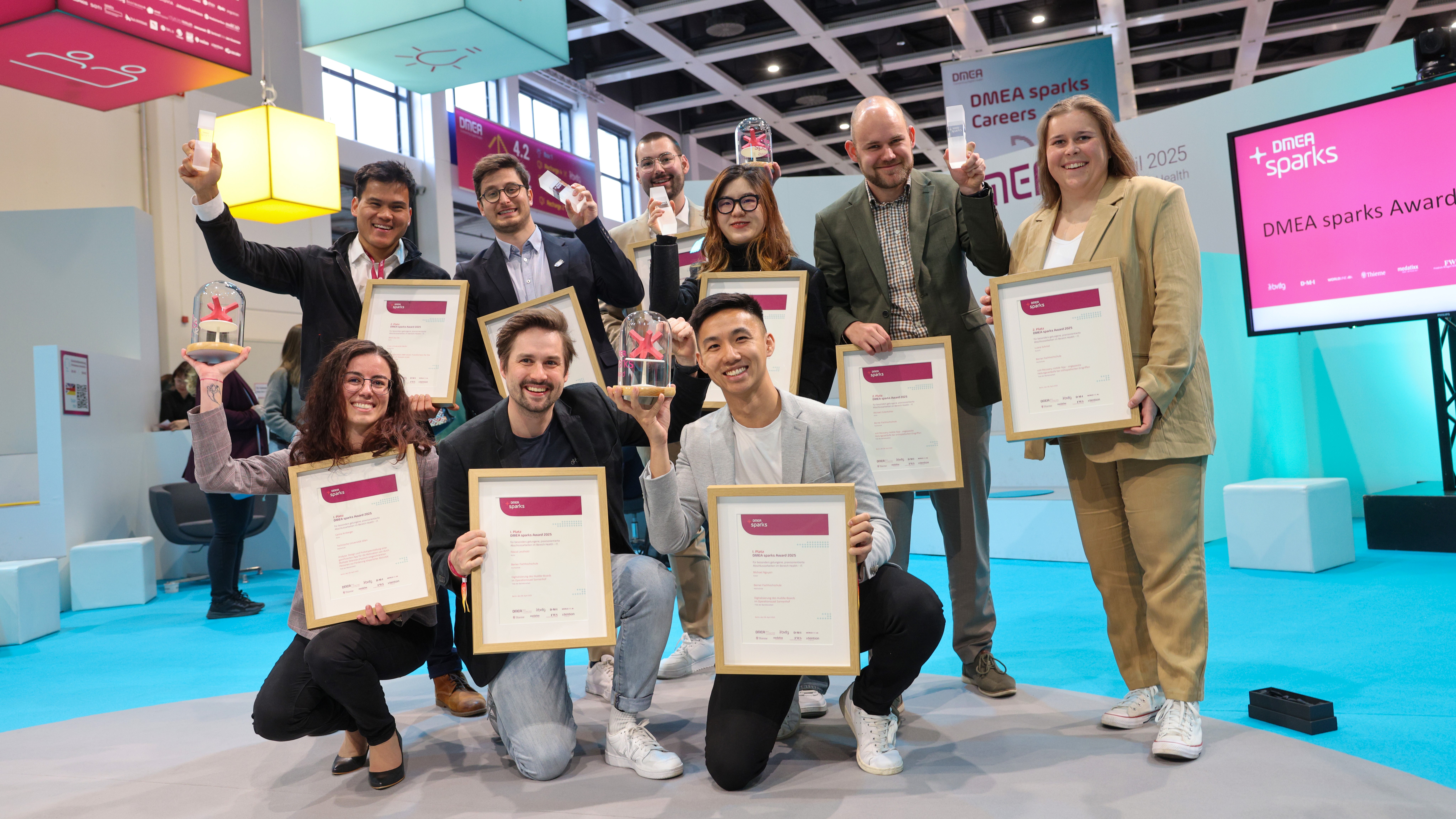 Gruppenbild der neun Gewinner des DMEA sparks Award 2025, die ihre Urkunden zeigen.